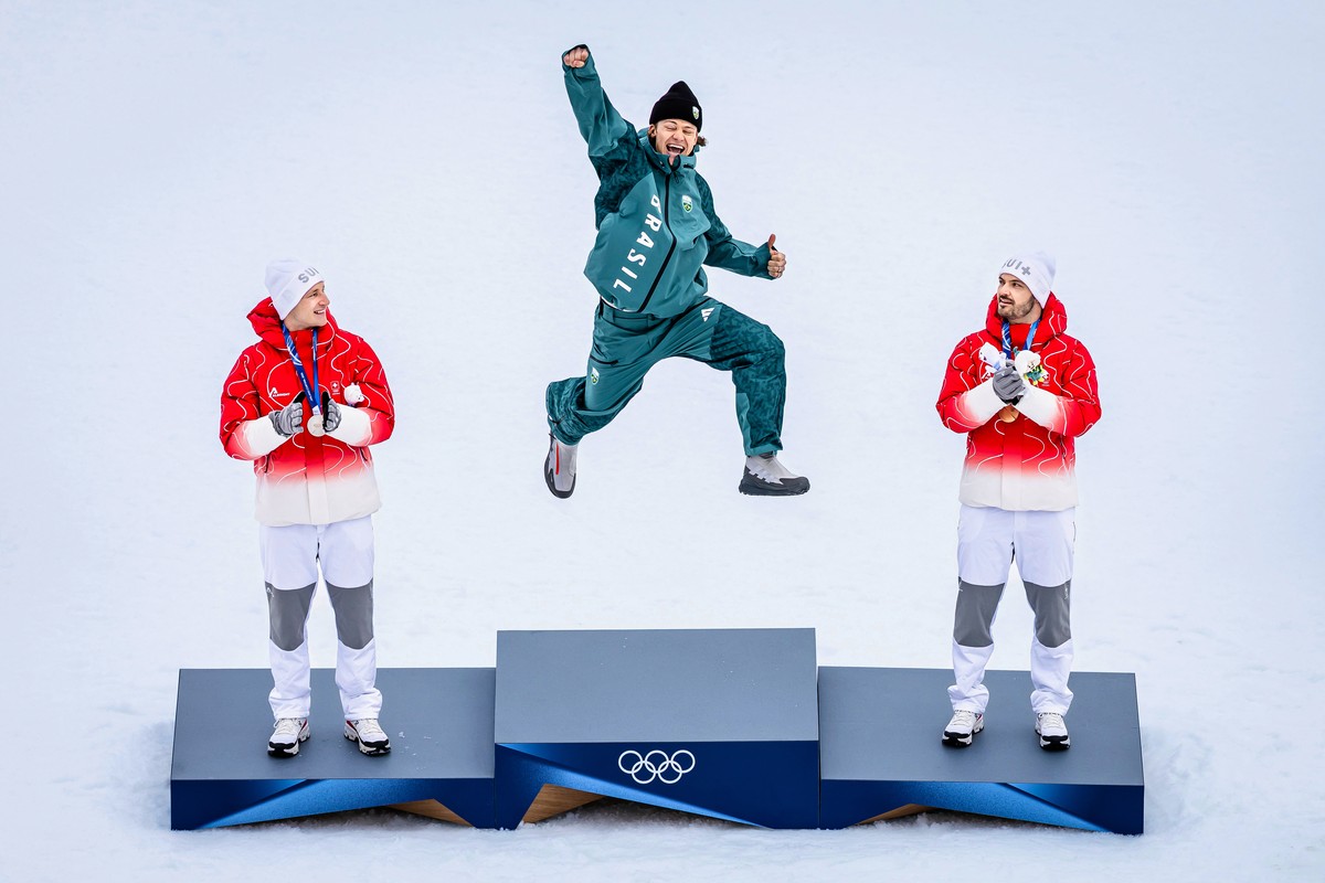 Brazil's Lucas Pinheiro Braathen, center, winner of an alpine ski, men's giant slalom race, jumps in celebration on the podium flanked by second placed Switzerland's Marco Odermatt, lef ...