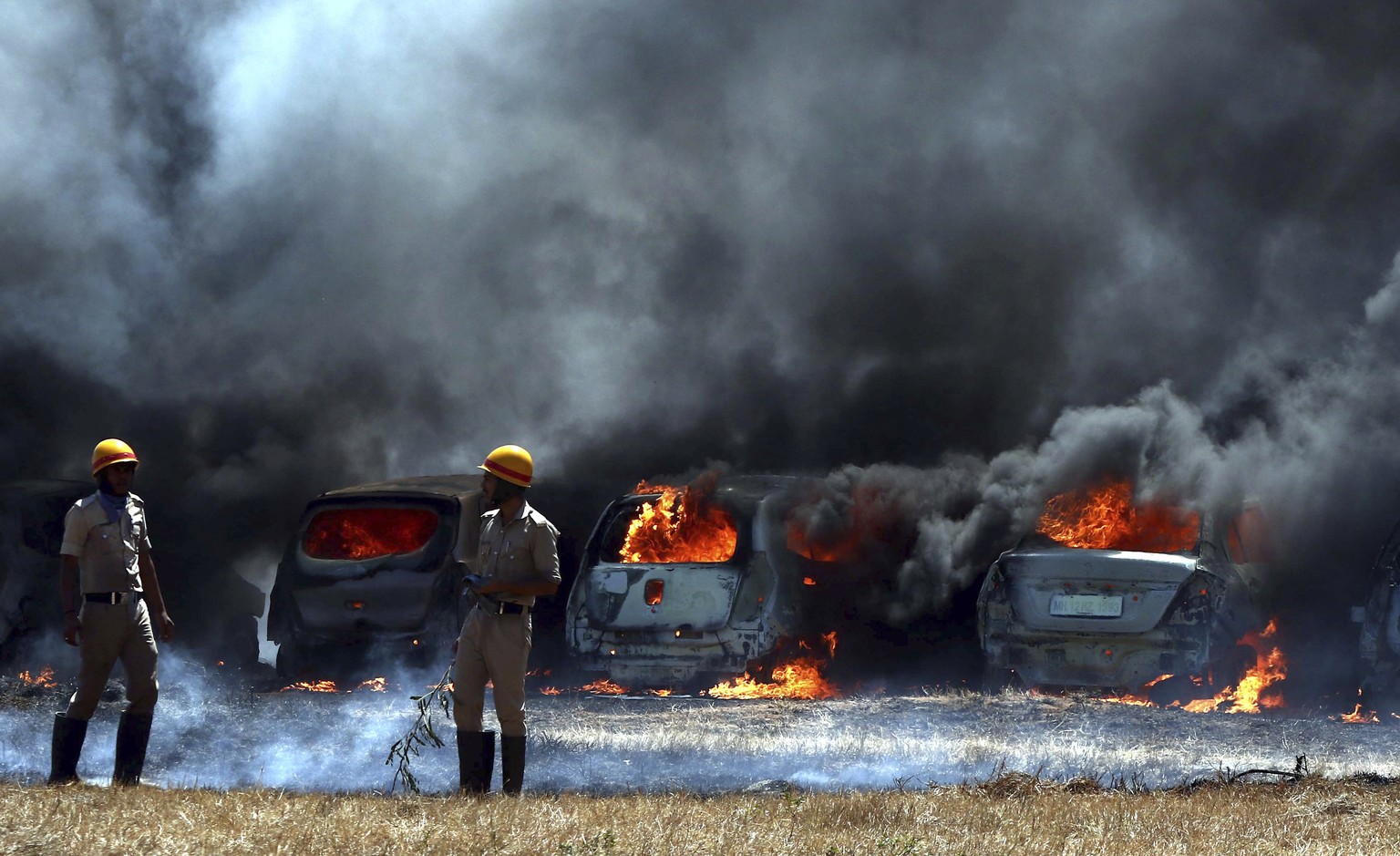 Firefighters stand next to burning cars after a fire broke out in a parking area outside Yelahanka air base, the venue of Aero India 2019 in Bangalore, India, Saturday, Feb. 23, 2019. The cause of the ...