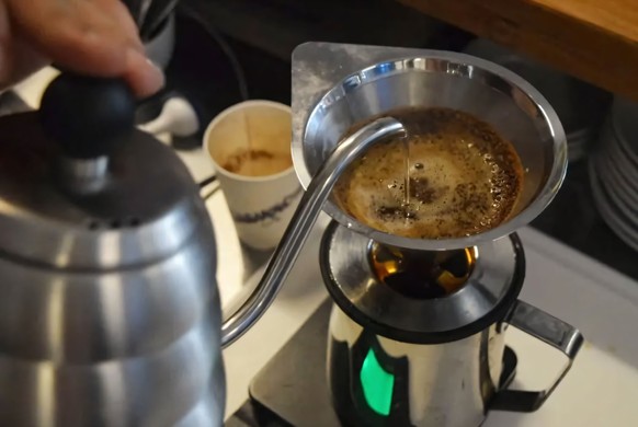 Barista pours hot water from gooseneck kettle into coffee filter on scale 28396250 RECORD DATE NOT STATED