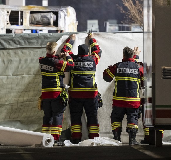 Firemen close off the area with covers in front of the charred shell of a postal bus which caught fire in Kerzers, Switzerland, Tuesday, March 10, 2026. According to the Fribourg cantonal police, seve ...
