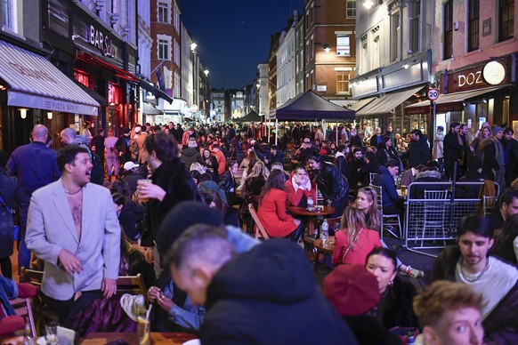 People sit at setup tables outside pubs in Soho, in London, on the day some of England's third coronavirus lockdown restrictions were eased by the British government, Monday, April 12, 2021. Pubs, sho ...