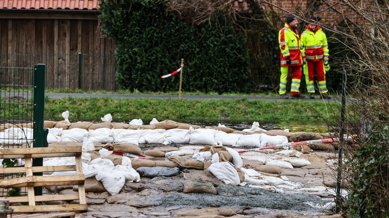 28.12.2023, Niedersachsen, Lilienthal: Helfer stehen hinter einem durchweichten Deichabschnitt an der W