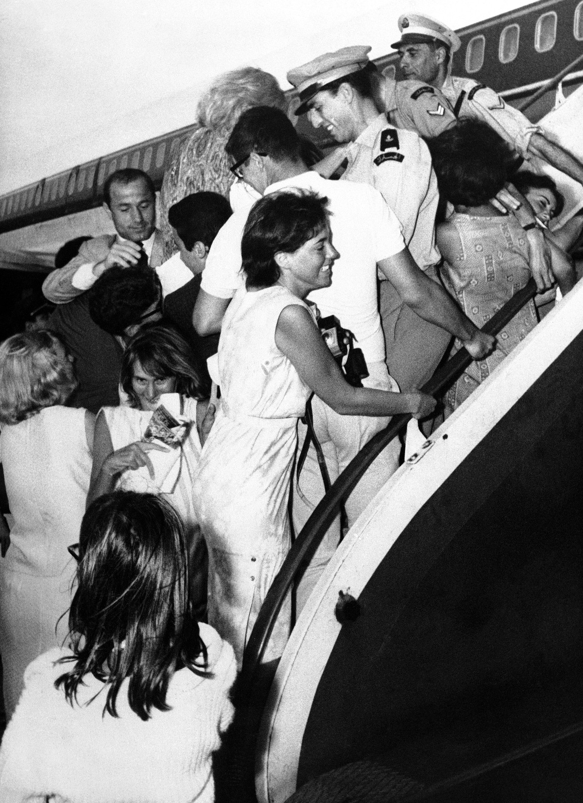 Three overworked policemen straddle the airplane steps to prevent frenzied Lebanese teenagers from clambering aboard the Beatles jet airliner during the pop quartets brief touchdown at Beirut Airport ...