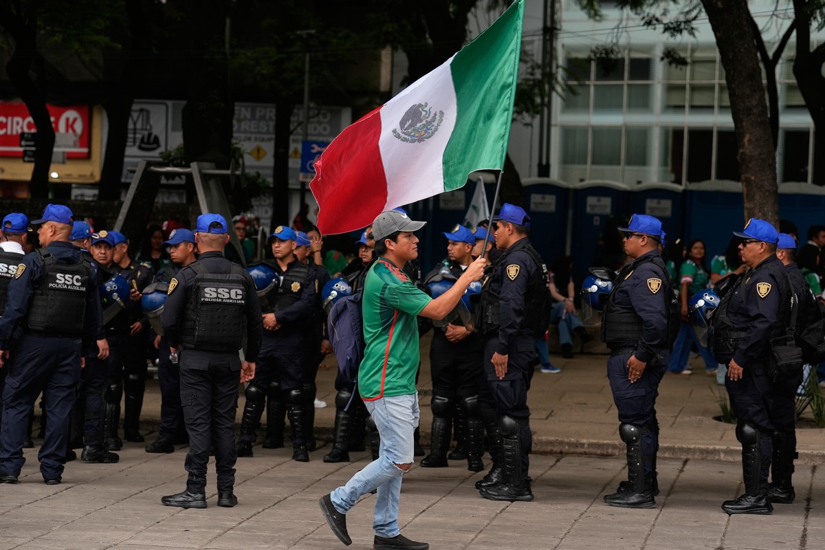 A soccer fan waving a Mexican national walks past a line of police at a watch party for the World Cup match between Mexico and Czechia on Reforma Ave., near the Angel of Independence monument in Mexic ...
