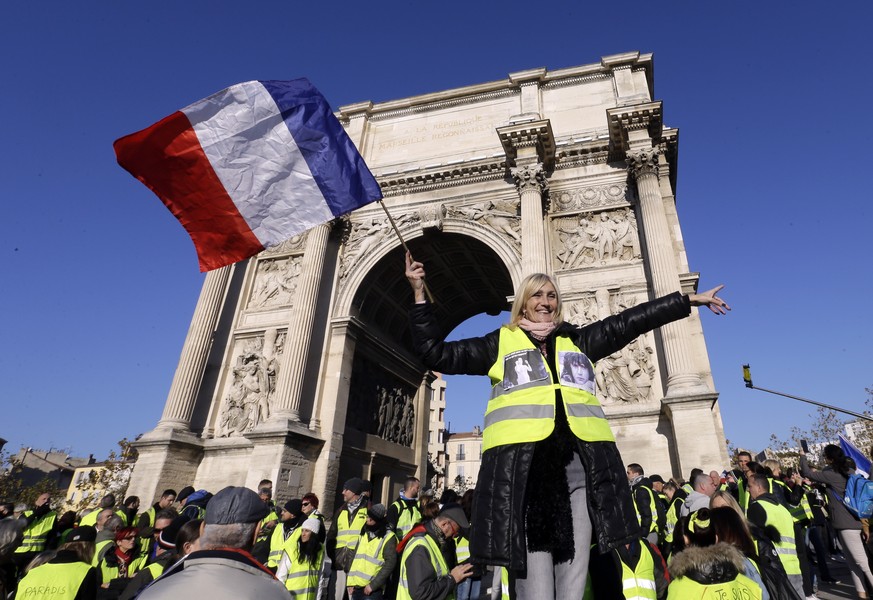A demonstrator wearing her yellow vest waves a national flag during a protest in front of the Arc de Triomphe of the Porte d&#039;Aix, in Marseille, southern France, Saturday, Dec. 29, 2018. The yello ...