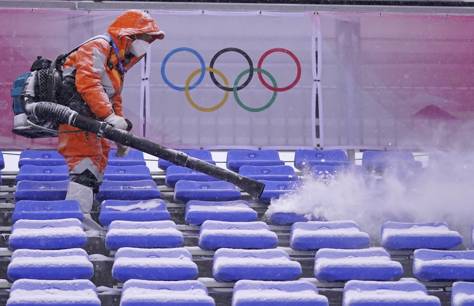 A worker clears snow from the seats in the finish area at the alpine ski venue at the 2022 Winter Olympics, Sunday, Feb. 13, 2022, in the Yanqing district of Beijing. (AP Photo/Robert F. Bukaty)