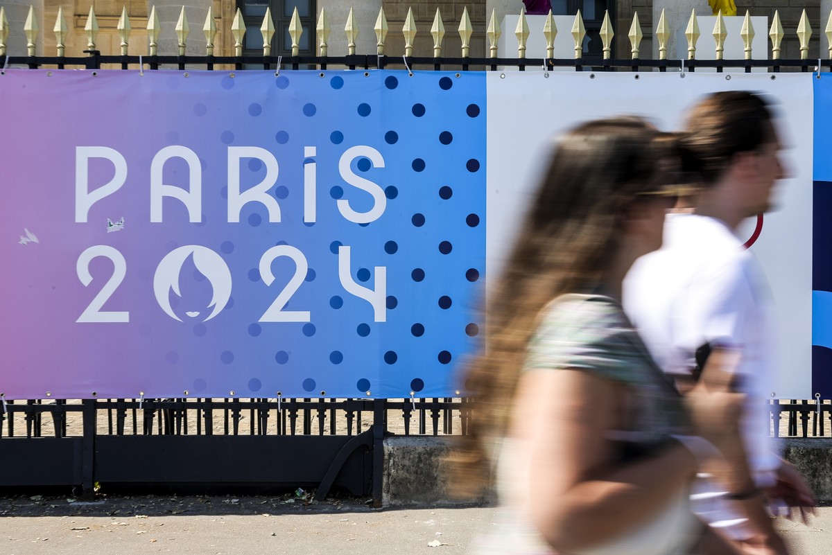 epa11483392 People walk past a sign with the Paris 2024 logo in Paris, France, 17 July 2024. From 18 to 26 July, the day of the Opening Ceremony of the Paris 2024 Olympic Games, security measures will ...