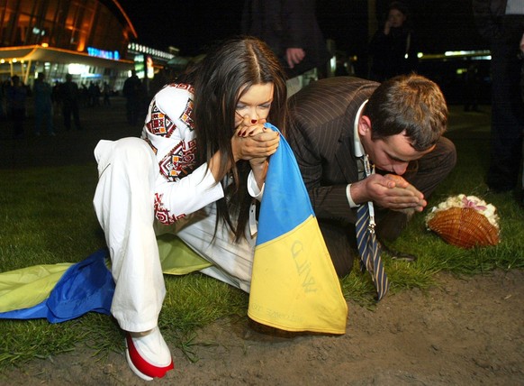 epa00192980 Ukrainian singer Ruslana Lyzichko (L) and Pavlo Gryshak, head of the Ukrainian delegation, kiss Ukrainian soil after arriving at Borispil airport near the Ukrainian capital Kiev late Sunda ...
