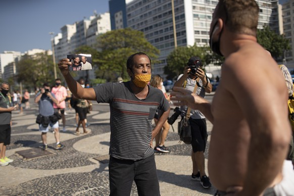 Marcio Antonio do Nascimento, left, holding a photo of his 25-year-old son Hugo do Nascimento who died from COVID-19, argues with a person who said the deaths related to COVID-19 are fake news, during ...