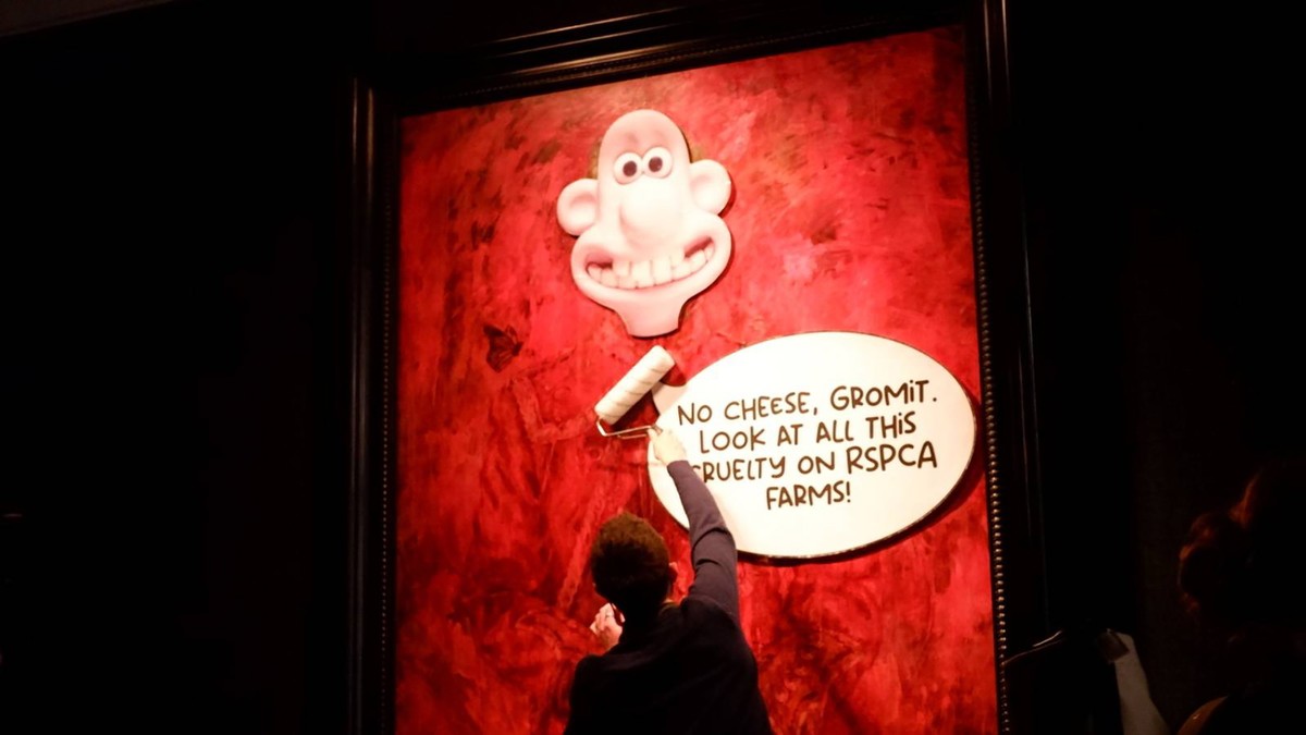epa11404202 A handout photo made available by animal rights group Animal Rising shows an activist affixing posters onto the painting of King Charles III at Philip Mould gallery in London, Britain, 11  ...