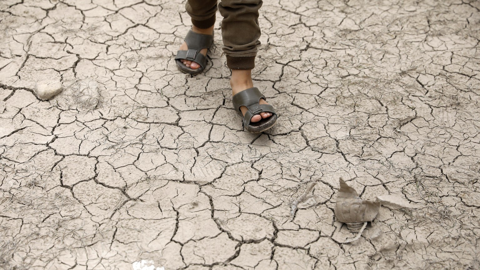 epa10817786 A boy walks on cracked ground at a drought-affected water reservoir during hot weather on the outskirts of Sana&#039;a, Yemen, 24 August 2023. The combination of a serious water shortage a ...