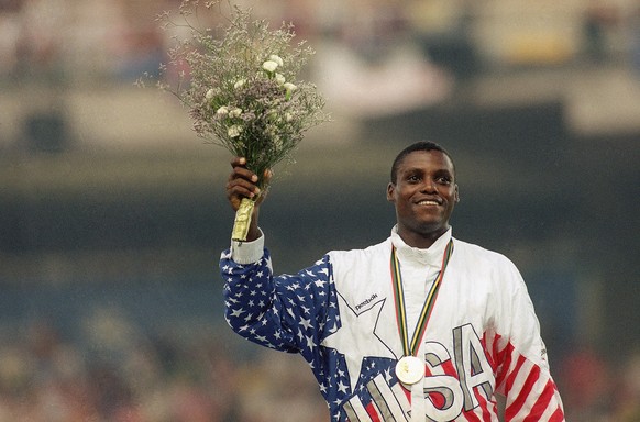 Three-time Olympic long jump champion Carl Lewis of Houston, Tex., holds up flowers Aug. 7, 1992 during medal ceremonies at the XXV Summer Olympics in Barcelona. Lewis beat out world record holder Mik ...
