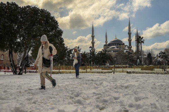 Tourists walk next to snow covered park next to Sultanahmet mosque after a snowfall in Istanbul, Turkey, Friday, March 11, 2022. (AP Photo/Emrah Gurel)