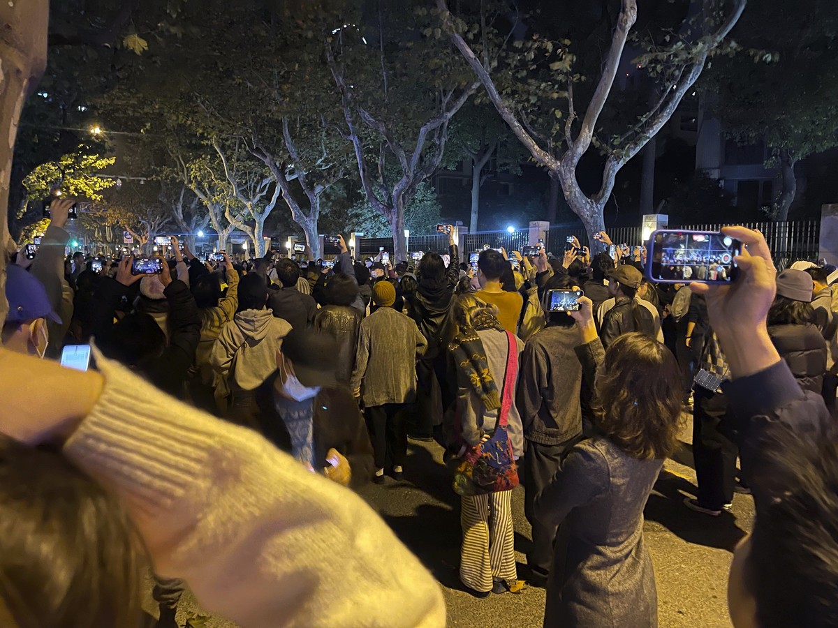 Residents record the scene as they mourn for the victims a recent deadly fire at a residential building in Urumqi city at a road sign of the Middle Wulumuqi Road or Middle Urumqi Rd and calls for free ...