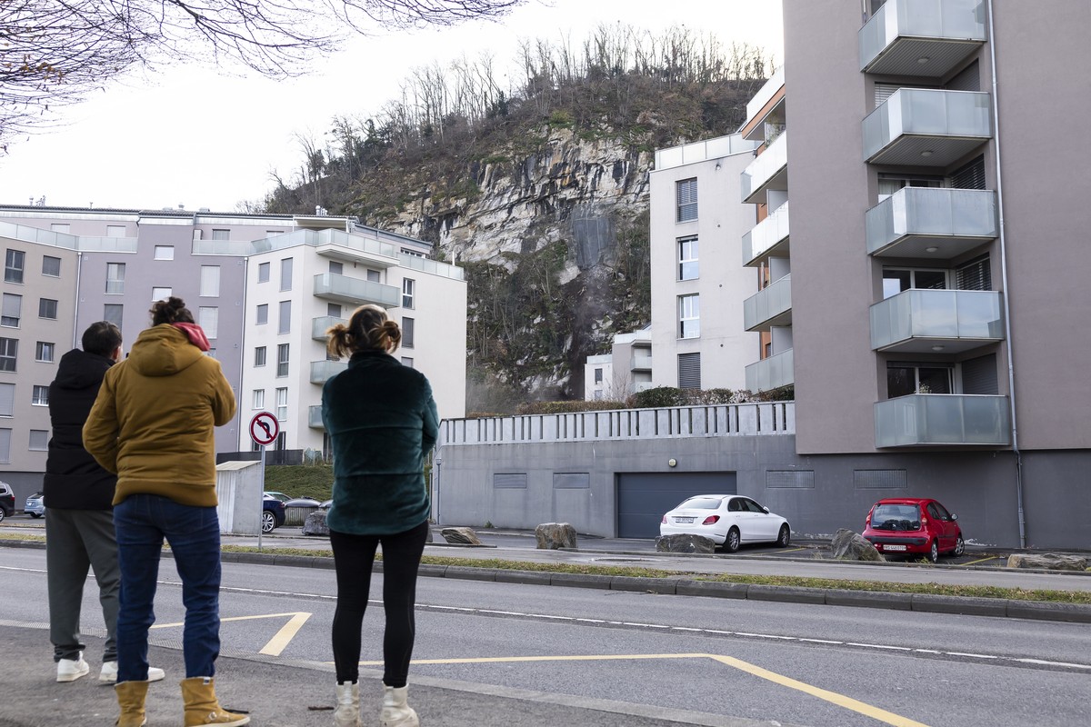 Des personnes regardent des blocs de pierre et de la terre tomber de la paroi lors du minage d'un bloc rocheux de la falaise de la Barme ce mardi 2 decembre 2025 a Collombey-Muraz. (KEYSTONE/Cyri ...