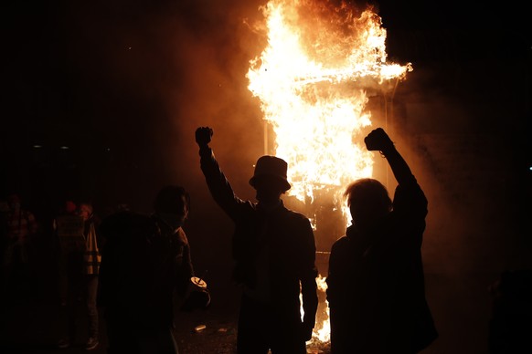 Youths raise the fists by a burning newsstand during a demonstration against a security law that would restrict sharing images of police, Saturday, Nov. 28, 2020 in Paris. Thousands of critics of a pr ...