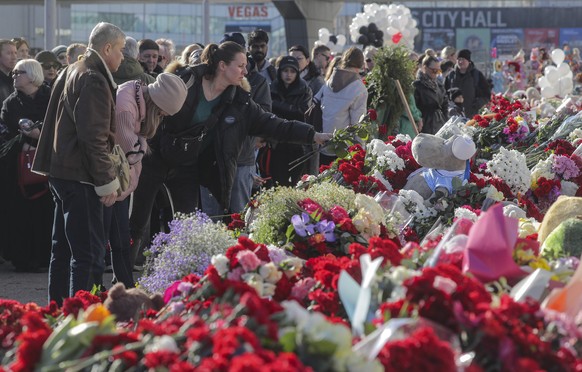 epa11242645 People mourn and carry flowers in front of the burned Crocus City Hall concert venue following a terrorist attack in Krasnogorsk, outside Moscow, Russia, 25 March 2024. At least 137 people ...