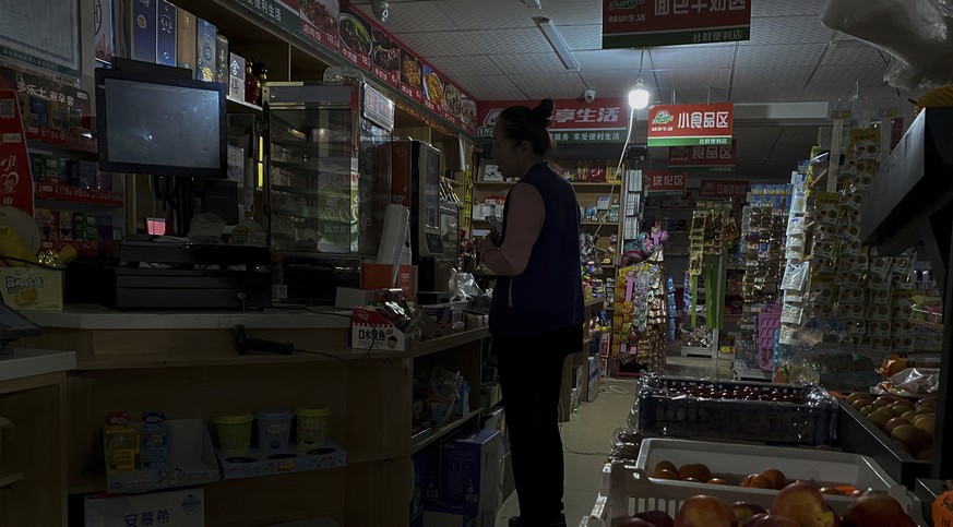 A woman buys groceries from a mini market using a light bulb powered by gasoline generator during a blackout in Shenyang in northeastern China's Liaoning Province, Wednesday, Sept. 29, 2021. Peop ...