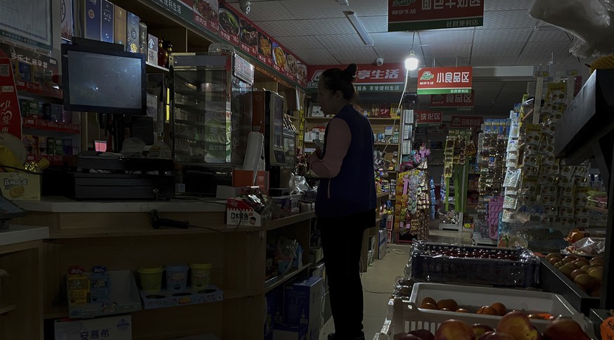 A woman buys groceries from a mini market using a light bulb powered by gasoline generator during a blackout in Shenyang in northeastern China&#039;s Liaoning Province, Wednesday, Sept. 29, 2021. Peop ...