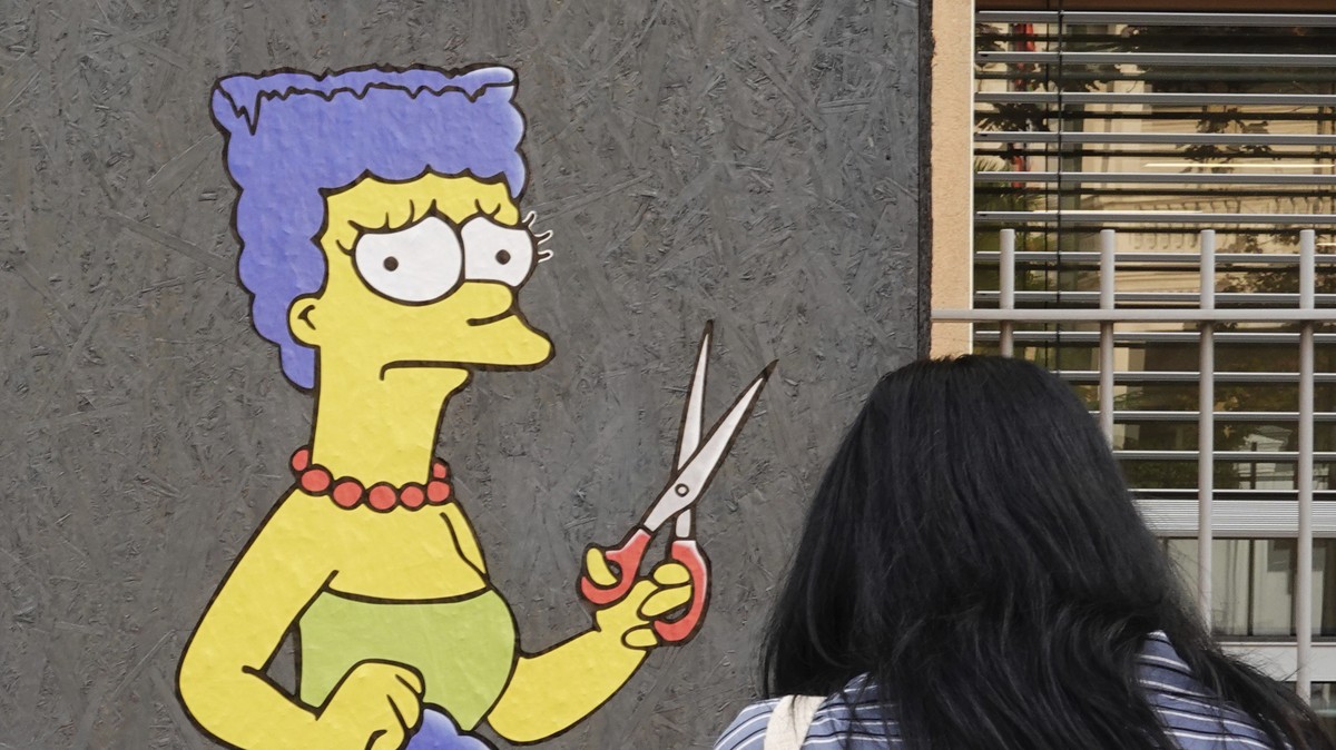 A woman takes pictures of a mural called "The Cut" by street artist aleXsandro Palombo depicting Marge Simpson, a character of the animated television series "The Simpsons" cutting ...