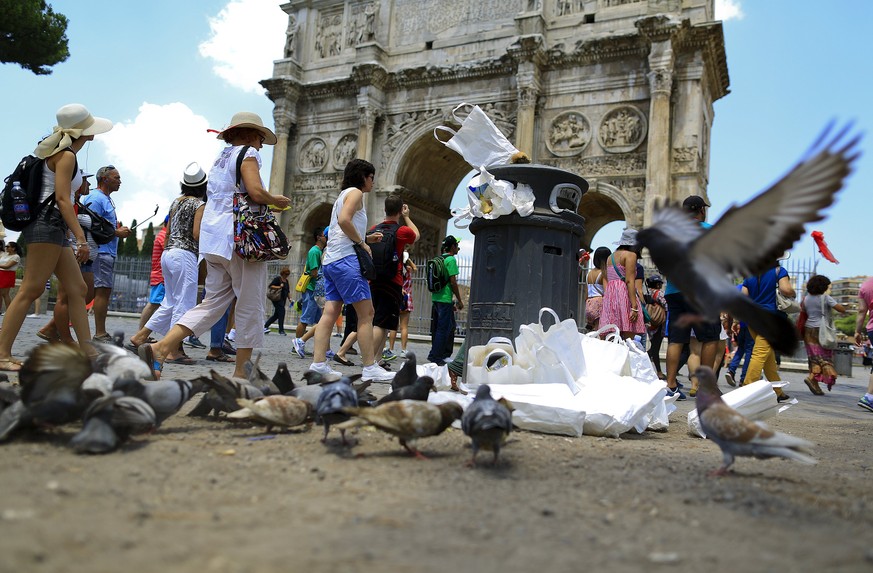 Tourists walk past the Arch of Constantine, as a pigeon flies next to a full garbage bin, in Rome July 12, 2015. Dirty and disorganised, Rome is once more in decline. City hall is paralysed by allegat ...