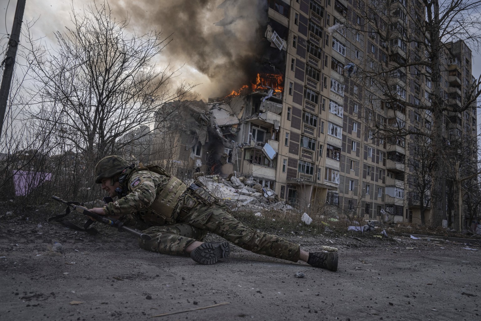 A Ukrainian police officer takes cover in front of a burning building that was hit in a Russian airstrike in Avdiivka, Ukraine, Friday, March 17, 2023. For months, authorities have been urging civilia ...