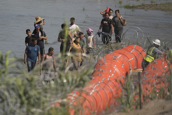 Migrants trying to enter the U.S. from Mexico approach the site where workers are assembling large buoys to be used as a border barrier along the banks of the Rio Grande in Eagle Pass, Texas, Tuesday, ...