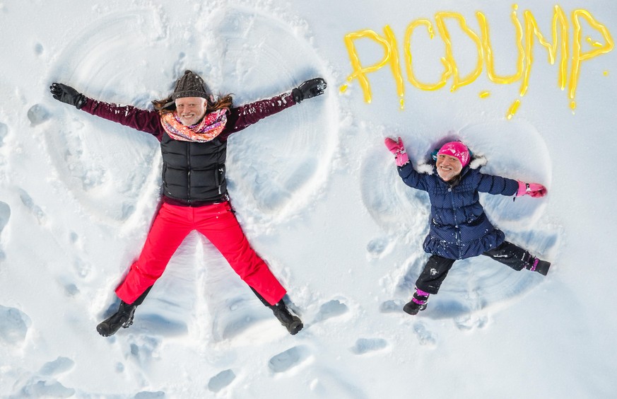 Happy family, mother and cute daughter making snow angel while lying on snow.