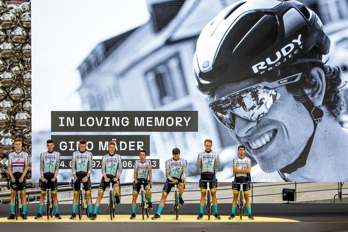 epa10718051 Cyclists of Bahrain Victorious team observe a minute of silence for their late teammate, Swiss rider Gino Maeder (pictured on screen), during the team presentation of the Tour de France 20 ...