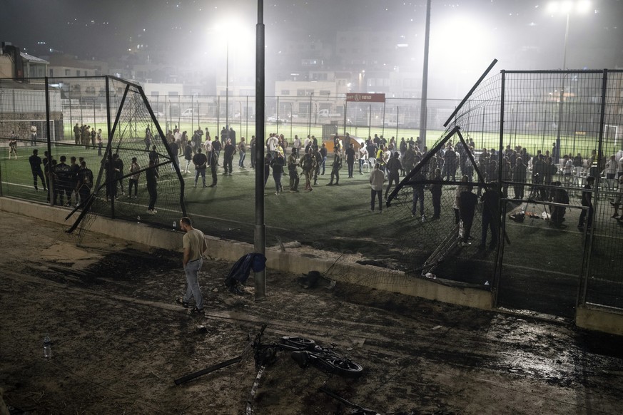 Residents and authorities stand at a soccer field that was hit by a rocket, killing multiple children and teenagers, in the Druze town of Majdal Shams, in the Israeli-annexed Golan Heights, Saturday,  ...