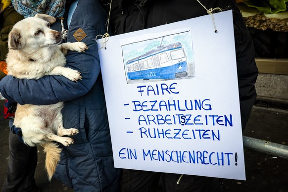 Hund Tuna neben einem Banner fuer Faire Bezahlung, Arbeitszeiten und Ruhezeiten waehrend eines Protestmarsches vom VBZ-Depot Oerlikon zum Sitz des Zuercher Verkehrsverbund ZVV, an einem Aktionstag der ...