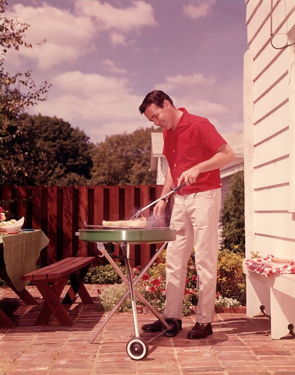 1960s MAN WEARING RED SHIRT COOKING STEAK OUTDOOR ON BACKYARD GRILL (Photo by H. Armstrong Roberts/ClassicStock/Getty Images)