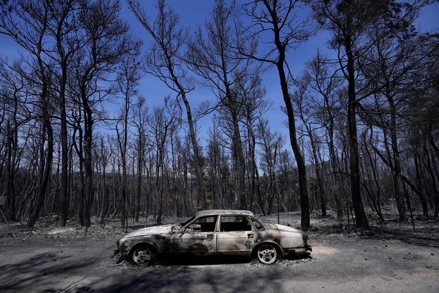 A burn car is seen at a road during a wildfire at Ipokratios Politia, in northern Athens, Greece, Saturday, Aug. 7, 2021. Wildfires rampaged through massive swathes of Greece's last remaining for ...