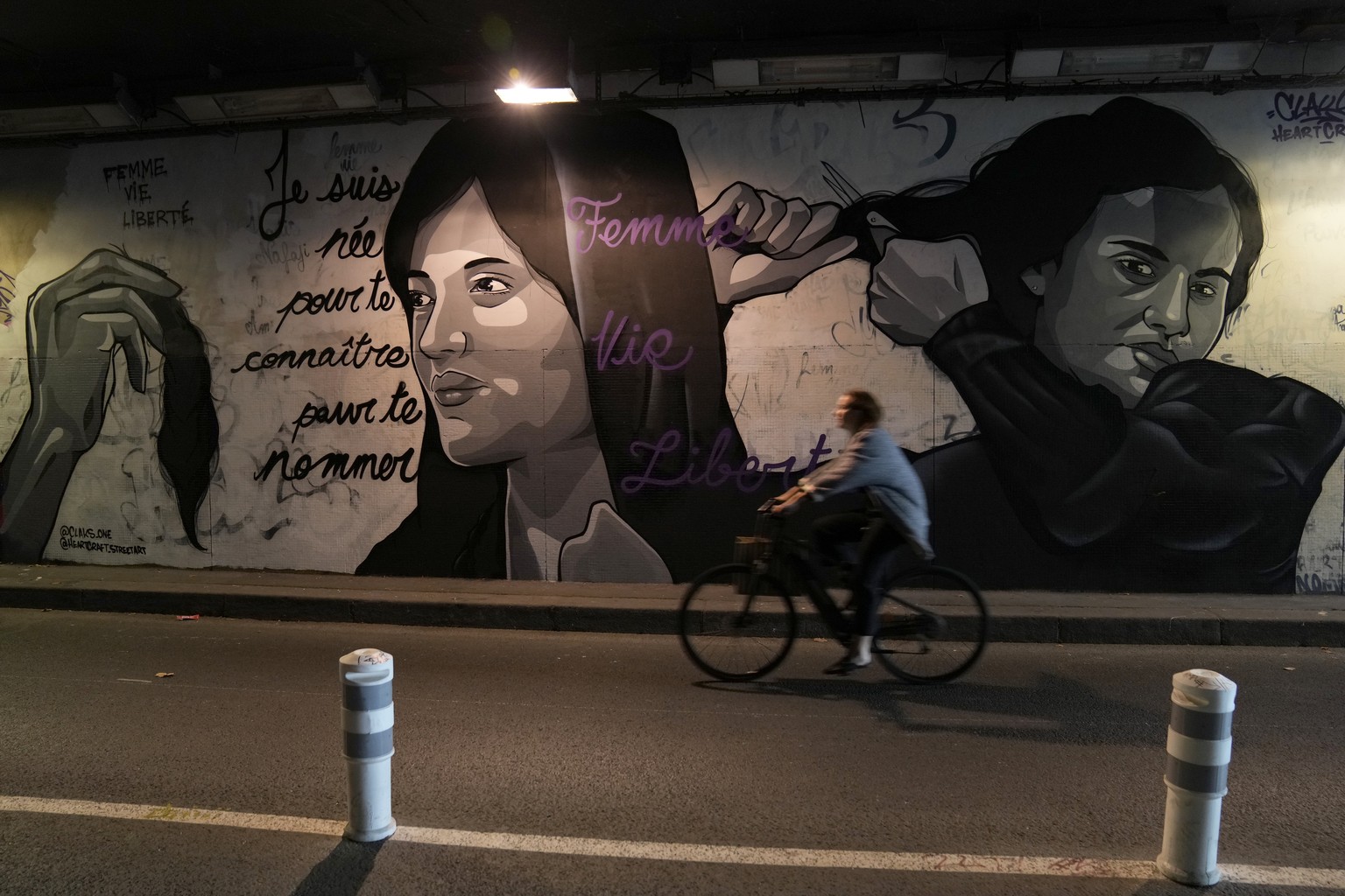 FILE - A woman rides bicycle front of a mural signed by Clacks-one and Heartcraft_Street art, depicting women cutting their hair to show support for Iranian protesters standing up to their leadership  ...