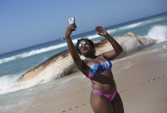 A woman poses for a selfie backdropped by the carcass of a humpback whale on Ipanema beach, in Rio de Janeiro, Brazil, Wednesday, Nov. 15, 2017. Biologist Rafael Carvalho said the whale appears to hav ...