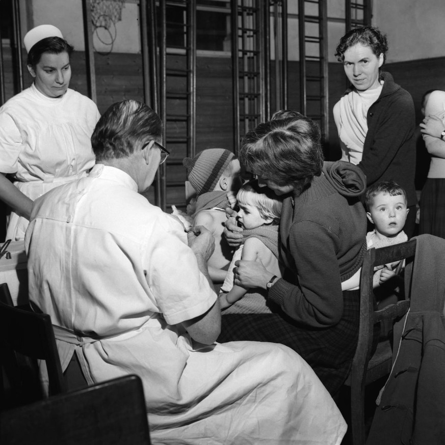 Bei einer freiwilligen Impfaktion der Bevoelkerung von Schaffhausen am 8. Januar 1962 impft ein Arzt ein Kind in den entbloessten Oberarm, waehrend eine Mutter mit ihren Kindern auf die Impfung warten ...