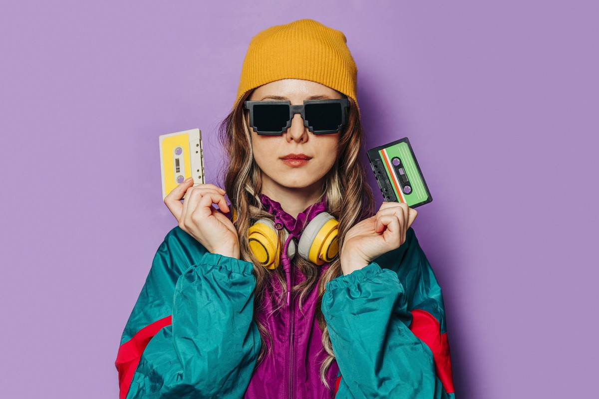 Woman in 80s style tracksuit holding music cassettes against a purple background model released, Symbolfoto, VSNF03117