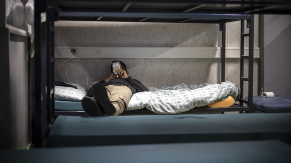 Ein Mann benutzt sein Mobiltelefon waehrend er in einem Schlafsaal auf einem Bett liegt, aufgenommen waehrend eines Medienrundgans im Bundesasylzentrum Zuerich, am Donnerstag, 27. Oktober 2022 in Zuer ...