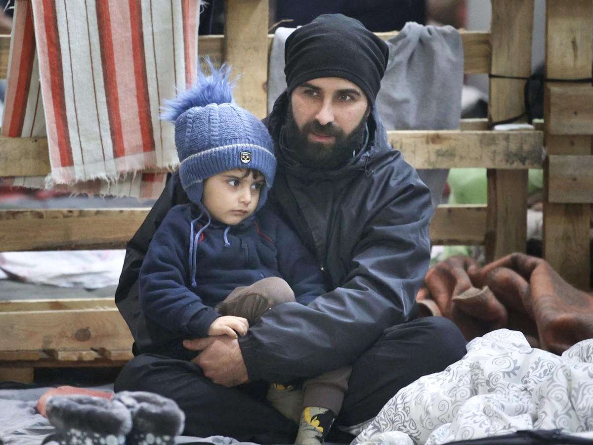 A man and his child rest inside a logistics center at the checkpoint "Kuznitsa" at the Belarus-Poland border near Grodno, Belarus, Sunday, Nov. 28, 2021. The West has accused Belarusian Pres ...