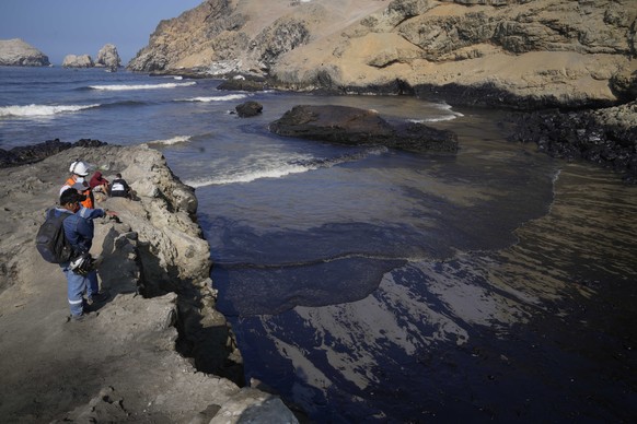 Workers look at the oil in the waters of Cavero Beach in Ventanilla, Callao, Peru, Tuesday, Jan. 18, 2022, after high waves attributed to the eruption of an undersea volcano in Tonga caused an oil spi ...