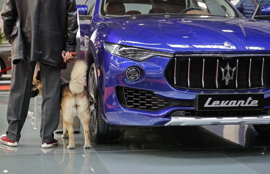 A man and his dog stand next to the Maserati Levante SUV at the Bucharest Auto Show in Bucharest, Romania, Thursday, Oct. 20, 2016. Romania&#039;s environment minister urged carmakers at the show open ...