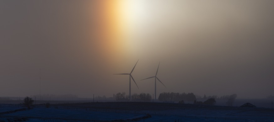 epa11078247 A sundog rises behind wind turbines outside Wellsburg, Iowa, USA, 14 January 2024. Sundogs appear on extremely cold days, when sunlight passes through airborne ice crystals. The cold tempe ...