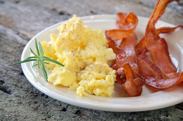Scrambled eggs with crispy bacon on a plate, and garnished with a fresh
sprig of Rosemary.