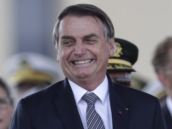 With the red plume of the helmet of an honor guard in the foreground, Brazils President Jair Bolsonaro smile during a military ceremony for the Day of the Soldier, at Army Headquarters in Brasilia, Br ...