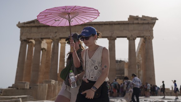 FILE - Tourists with an umbrella walk in front of the Parthenon at the ancient Acropolis in central Athens, June 12, 2024. June 2024 was the hottest June on record, according to Europe&#039;s Copernic ...