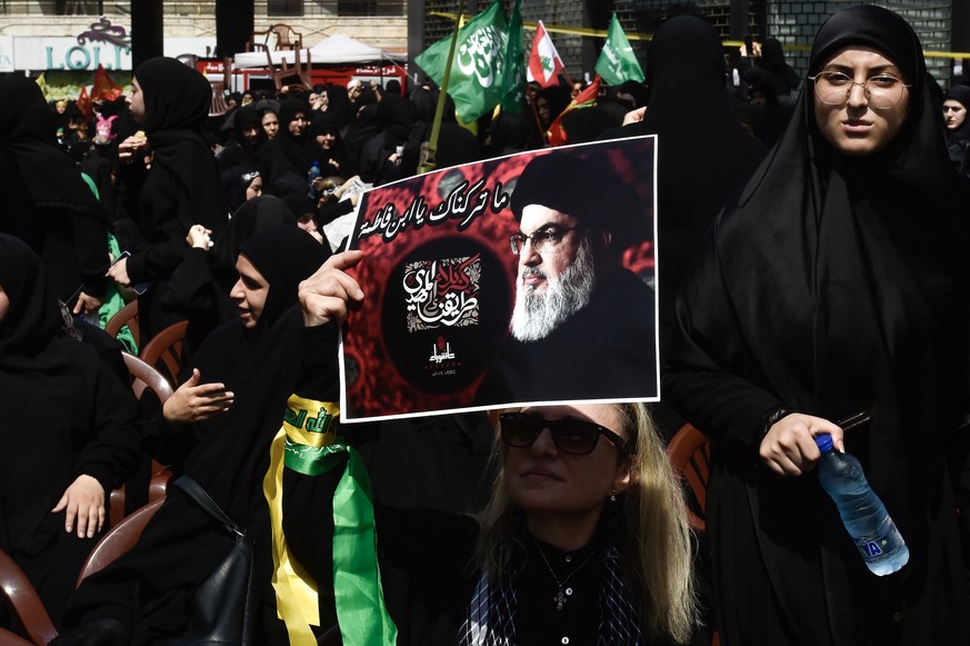 epa10775038 A Hezbollah supporter holds a poster with the portrait of Hezbollah leader Hassan Nasrallah as she listens to his speech during an Ashura Day procession in southern Beirut, Lebanon, 29 Jul ...