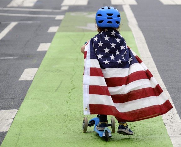 Two and a half year old Zacky Kaplan rides his scooter while draped in the American flag as he makes his way along the parade route during the Santa Monica Fourth of July Parade on Thursday, July 4, 2 ...