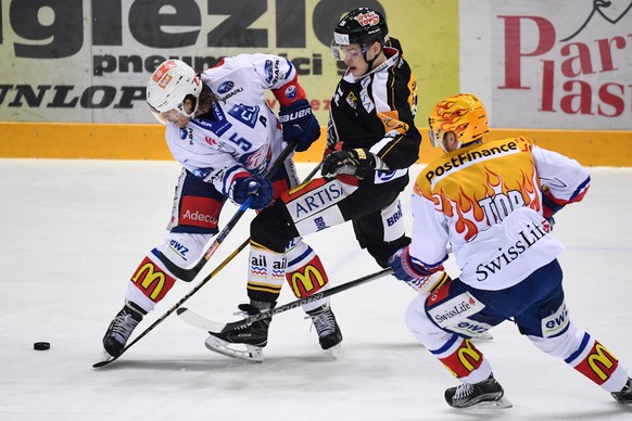 Zurich's player Severin Blindenbacher, left, fights for the puck with Lugano’s player Gregory Hofmann, center, during the second leg of the Playoffs quarterfinals game of National League A (NLA) Swiss ...