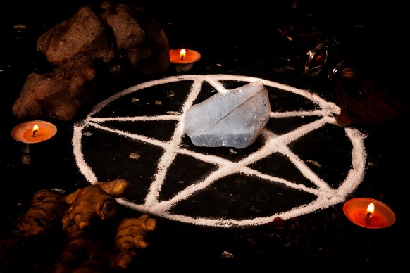 Pentagram made of salt, a symbol used for protection, surrounded by candles, herbs and spices in dim moody lighting.