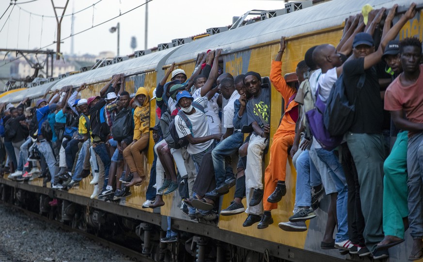 Train commuters hold on to the side of an overcrowded passenger train in Soweto, South Africa, Monday, March 16, 2020. South Africa will revoke nearly 10,000 visas issued this year to people from Chin ...